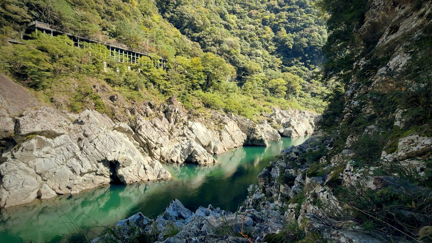 The emerald river in Oboke Gorge between grey rock walls, with a covered railway gallery high on the green slope.